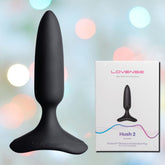 A black Lovense Hush 2 Vibrating Butt Plug - XS by Lovense is showcased alongside its packaging, which features an image of the product and colorful wave designs on a light background. Enjoy intense vibrations with this Bluetooth remote-controlled device that combines style with functionality.